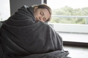 sick-woman-sitting-sofa-with-closed-eyes-embracing-knees-min
